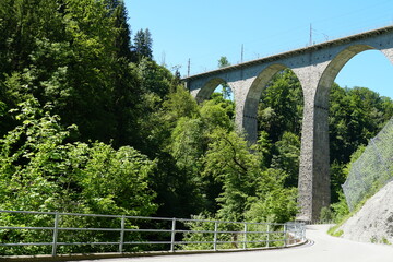 Viaduct railway bridge and a road with metal railings underneath, surrounded by fresh springtime nature. The bridge is on St. Gallen bridge hiking trail in Eastern Switzerland.