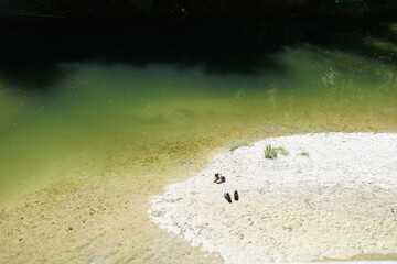 A small river nay with sandy banks on anright summer day. Two pairs of shoes on the bank imply two...