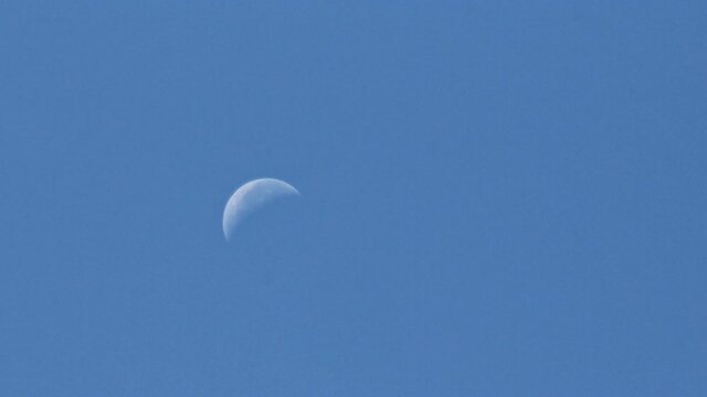 A crescent moon drifts along a blue sky in time-lapse. Ends with white, wispy clouds filling the frame.