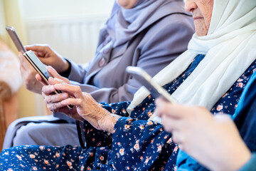 Happy arabic muslim grandmother and grand daughter and mother sitting togther on couch using technology