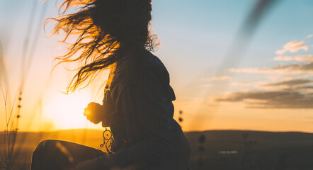 Silhouette of a young woman with her hair in motion backlit by gorgeous golden sunset sky
