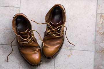 Pair of old and worn reliable brown boots shot from above on a tiled floor.