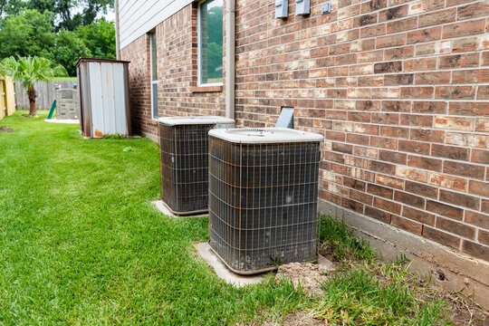 Two Older HVAC Air Conditioner Systems Next To Brick Home With Copy Space.