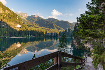 A path with a wooden fence climbs steeply beside the Braies lake