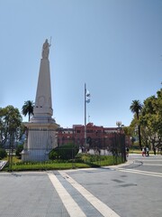 Monument in the middle of a square with a historical building in the background.