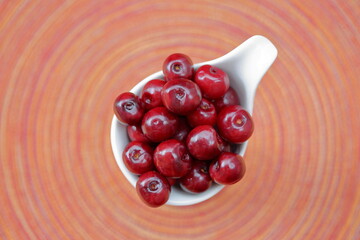 Fresh cherries in a white bowl bowl agianst colorful background concentric vibrant circles in soft focus flat lay


