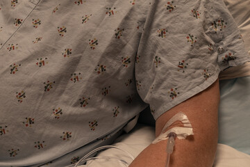 Close view of an IV in a mans arm, drab hospital gown copy space, horizontal aspect