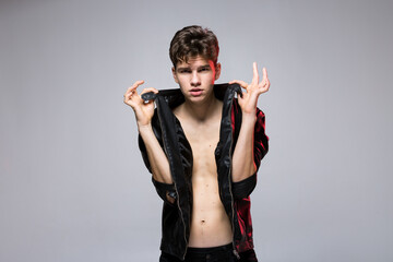 Fashionable Handsome young man in leather jacket posing in the studio against the background of the wall. Portrait of a young gay man in black clothes on a naked torso. Thin tall Caucasian Male Model