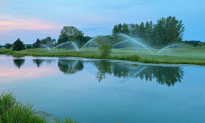 sunrise water sprinklers on golf course pond reflections