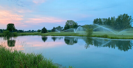sunrise water sprinklers on golf course pond reflections - obrazy, fototapety, plakaty