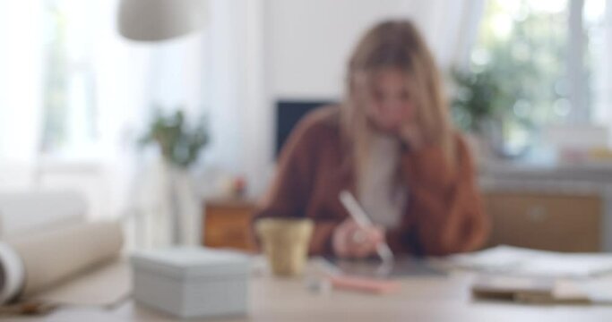Female person drawing on tablet and creating picture while sitting at her cosy workplace. Woman graphic illustrator using stylus and pad while working on her project. Blurred
