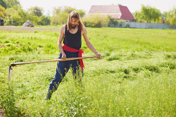 Rural farmer on summer meadow mowing grass with classic scythe. Traditional way of mowing the grass with the scythe.