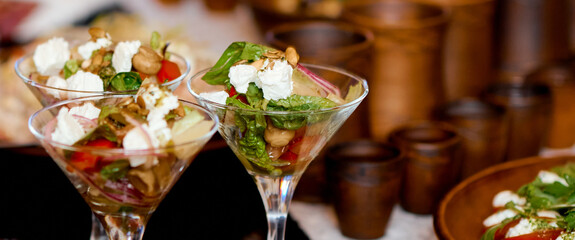Fototapeta premium Three servings of salad in martini glasses on the table. Clay utensils in the background. 