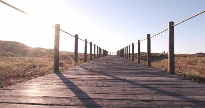 Wooden boardwalk over sand dunes in Vila do Conde protected nature reserve, Portugal. Low angle, walking forward, sun on left.