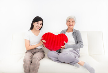 Obraz premium old asian female and young female rest on sofa, old woman hug red heart pillow, they feeling happy and smile, mother's day and family time