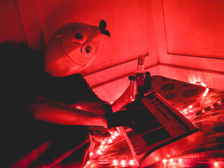 Bizarre portrait of a guy with lemon mask on a old mattress playing the keyboard, with neon red lights