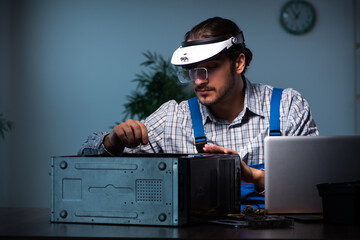 Young male technician repairing computer in workshop at night