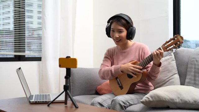 Teach guitar online, Asian female teacher teaches how to play an instrument through live streaming.