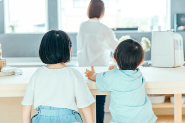 Obraz premium 家の中で子供二人が並んで母親の背中を見ている 朝食 食卓 シングルマザー