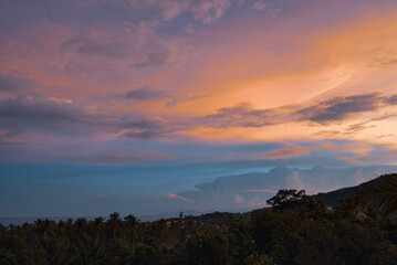 Colorful sunset over forest, village, sea and mountains on a tropical island. View from the top.