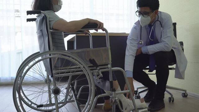 asian doctor exam woman patient who is sitting in the wheelchair and get leg injury from accident. healthcare and medical concept