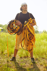 Close-up of a young Caucasian man with a slackline rope in his hands in the forest at sunset.