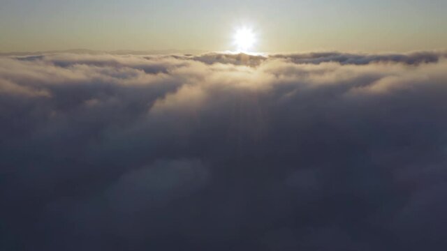 Camera is raising above from the thick fog above the beautiful ocean of clouds at sunrise. Sun is rising above the endless sea of clouds until the horizon. Amazing nature landscape, 4K drone in sky