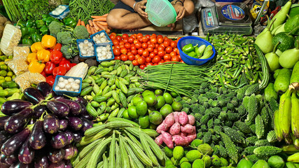 Fresh green vegetables on display for sale with view of the shopkeeper at a local market store at...