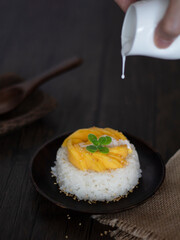 Pouring Coconut Milk Over Thai Mango Sticky Rice Rustic Shot. Street Food Mango Glutinous Rice Dark Food Photography.