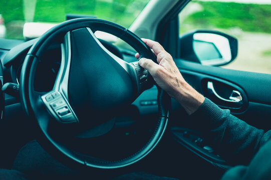 The hand of a senior man on a steering wheel