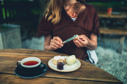 Young mother with baby preparing a scone with jam and creaam