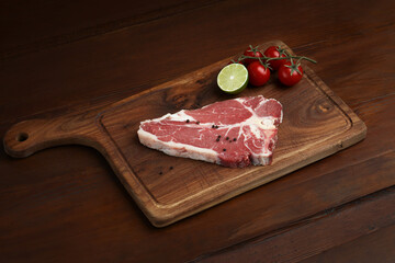 Fresh raw t bone steak on wooden Board  background with tomato, pepper, kiwi, and rosemary in a...