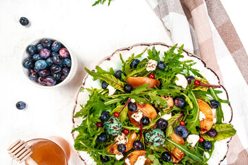 Arugula and peaches salad. Vegetarian gourmet salad made of caramelized grilled peaches slices, arugula leaves, goat cheese on a light background, top view
