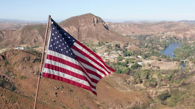 American Flag blowing in the wind with mountains landscape and blue sky on a background. USA American Flag. Waving United states of America famous flag in front of green suburban. American concept.