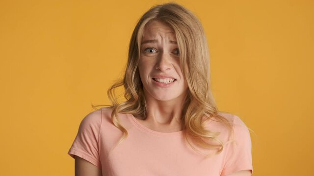 Young afraid blond girl scaredly closing eyes over colorful background. Fear expression