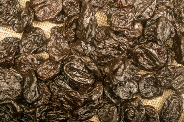 Dried prunes in bulk on burlap with a rough texture. Close up.