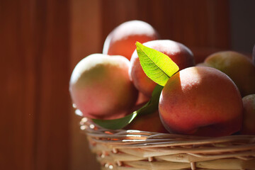 Close up of fresh peaches in a basket. Sun light shining on them. Rustic wooden background. For concepts related to food, fruit, agriculture, farming, nutrition, freshness, and health.