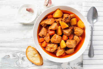Pork meat stewed with potatoes, carrots and spices (hungarian goulash). on white wooden background top view