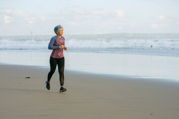 fit and happy middle aged woman running on the beach - 40s or 50s attractive mature lady with grey hair doing jogging workout enjoying fitness and healthy lifestyle