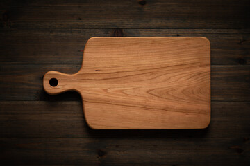 Handmade cherry wood cutting board on dark wood table, cherry wood cutting board texture background.