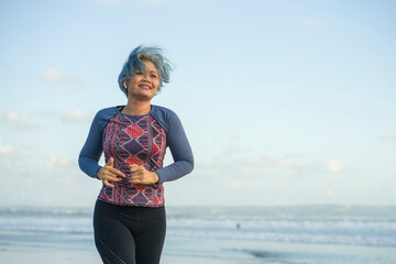 fit and happy middle aged woman running on the beach - 40s or 50s attractive mature lady with grey hair doing jogging workout enjoying fitness and healthy lifestyle