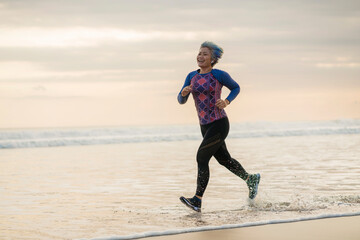 fit and happy middle aged woman running on the beach - 40s or 50s attractive mature lady with grey hair doing jogging workout enjoying fitness and healthy lifestyle