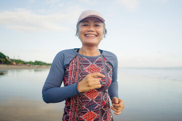 fit and happy middle aged woman running on the beach - 40s or 50s attractive mature lady with grey hair doing jogging workout enjoying fitness and healthy lifestyle