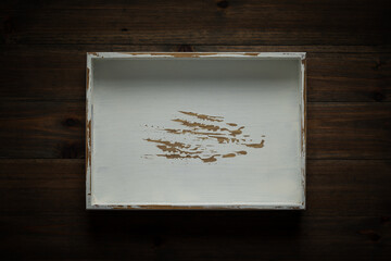 An empty white handmade wooden tray on dark wood tabletop
