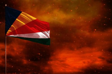 Fluttering Seychelles flag mockup with blank space for your text on crimson red sky with smoke pillars background. Troubles concept.