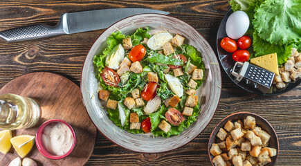 Plate with delicious fresh Caesar salad and ingredients for its preparation. Top view