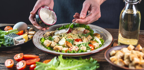 Chef is dressing the Caesar salad with a special fresh sauce. Concept of the process of cooking a delicious dish