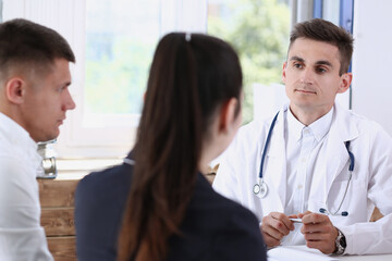 Male family doctor listen carefully young couple in office portrait. Motherhood and child delivery,...