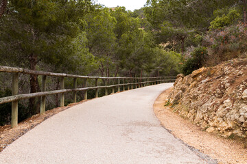 Asphalt road with wooden railings in a green nature park Sierra Gelada.