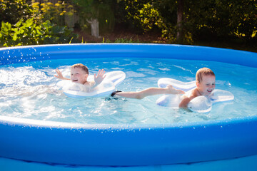 Two boys are happily swimming in the pool on inflatable circles in the form of a star. The concept of summer and recreation by the water.